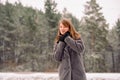 A girl with a sweet smile in frosty weather against the background of a forest with tall trees. Winter scenery. Royalty Free Stock Photo