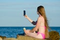 Girl in swimsuit with ice cream in hand on rocky beach makes selfie phone against the sea Royalty Free Stock Photo