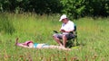 A girl in a swimsuit is sunbathing on the lawn. Next to her in a picnic chair, a man sits and plays in the smartphone. Take a bott