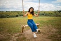 Girl swings in a calm sunny day. The lady sits on a wooden swing and looks at the field.