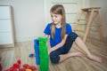 A girl in a blue T-shirt in a children`s room builds towers from blue and green cubes