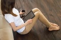 The girl is sitting on the floor with a tablet in her hands reading news, a cup of coffee holds in hands