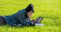 Girl with tablet, lying on green grass and writing on tablet bores from homework