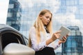 Girl with tablet near car in front of skyscraper