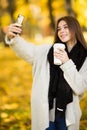 Girl take selfie on phone with cup of coffee on yellow sunny park