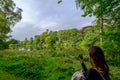 A girl takes a photo of the beautiful summer landscape of trees foliage and a Pond in West Yorkshire outside Leeds, England