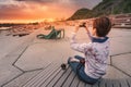 Girl takes photos of a beautiful sunset on her phone while sitting on a bench in a city Park on the river embankment Royalty Free Stock Photo