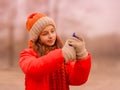 Teenage girl looks into a smartphone in autumn or winter in the park. The girl takes a selfie