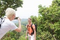 Girl Taking Photo Of Guy With Backpack Posing Over Mountain Landscape On Cell Smart Phone, Trekking Young Man And Woman Royalty Free Stock Photo