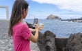 Girl taking a picture of the coffee in from of the sea with her cellphone. Mug for take away. Photography with phone to coffee cup