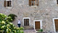 Girl taking picture with smart phone in the old town with stone facade of a house and wood windows. White sweater in mediterranean