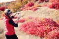 Girl taking pictures of bushes with autumn leaves