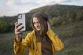 Girl taking selfie on smartphone on mountain background. Young woman in yellow jacket walk of autumn forest Royalty Free Stock Photo