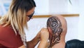 A girl, tattoo master, mehendi artist makes drawing of henna tattoo on scalp of bald Caucasian man, shoulder, neck.The