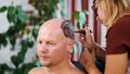 A girl, tattoo master, mehendi artist makes drawing of henna tattoo on scalp of bald Caucasian man, shoulder, neck.The