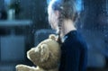 Girl with Teddy Bear Behind Window Covered by Rain Drops Royalty Free Stock Photo