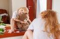 Girl with teddy bear looking through near mirror