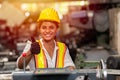 Girl teen worker with safety helmet show thumb up working as labor in industry factory with steel machine