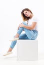 Girl teenager in blue jeans sits on cube in white studio