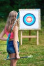 Girl teenager with bow and arrows in front of target