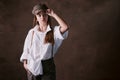 Girl teenager in a hat with a visor in a white shirt and trousers. studio brown background, fashion