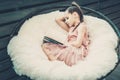 Girl teenager in a pink dress sitting in a chair on a white fur plaid and reading a book. Royalty Free Stock Photo