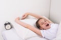 girl teenager with prosone pulls her arms up, in bed next to the alarm clock