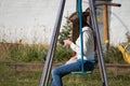 Girl teenager in a white jacket sitting on a swing with a mobile phone in their hands in the courtyard Royalty Free Stock Photo