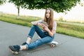 Girl teenager 9-11 years old, sits on board in hands of phone. In summer in city in casual jeans and a pink T-shirt Royalty Free Stock Photo