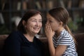 Girl telling secret to middle aged 60s grandma, whispering in ear