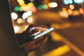 Girl texting finger on screen smartphone on background illumination glow bokeh light in night atmospheric city, hipster using in f Royalty Free Stock Photo