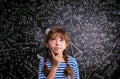 Girl thinking, finger on cheek, blackboard with mathematical sy