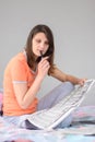 Girl thoughtfully reads newspaper ads while sitting on bed at home