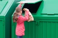 Girl throws out a paper bag in a green dumpster