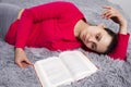 Girl is tired of reading book lying on bed. Attractive young brunette woman lies on bed with book in bedroom Royalty Free Stock Photo
