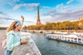 Girl tourist in a hat standing on a bridge and waving to a river cruise sailing by Seine river in Paris