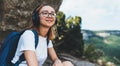 Girl tourist listens to music with headphones and plans walk in mountains in fresh clear air, young tourist dreamer in glasses Royalty Free Stock Photo