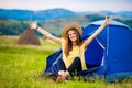 Girl tourist meets morning with outstretched arms in tent with beautiful mountains view