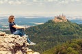 Girl tourist sitting on cliff looks at Hohenzollern Castle on mountain top, Germany Royalty Free Stock Photo