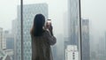 Girl tourist standing at the window and taking photo on a mobile phone view of a skyscraper height in Kuala Lumpur Royalty Free Stock Photo