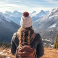 A girl tourist in a warm hat, dressed in a warm winter jacket with a backpack admires the mountains