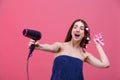 The girl is in a towel and with hair curlers, directs the hair dryer by herself. On a pink background.