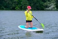 Girl in a tracksuit kneels on a surfboard and holds a paddle. Front View Photo