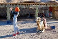 A girl in a tracksuit and orange arafatka takes a selfie against a camel