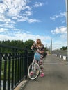 A girl in a tracksuit posing on a bicycle. Drinks water from a plastic bottle. Stands near the railings of the road bridge