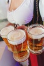 Girl in a traditional dress with a big breasts and deep neckline holds full mugs of beer.