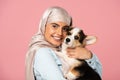 Girl in traditional scarf holding little puppy, isolated on pink