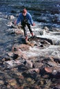 Girl traveler crossing a mountain fast river over a crossing over rocks