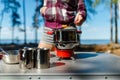 Girl traveler prepares food on portable gas stove, on a folding table on the background of camping in forest. Women's hands inter Royalty Free Stock Photo