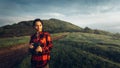 Girl Traveler In Red Plaid Shirt With Binoculars In Hands Looks Into Distance On Landscape Background. Scout Travel Adventure Conc